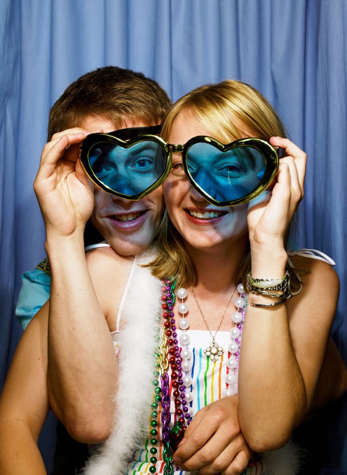 Young couple in photo booth, woman holding heart shaped glasses